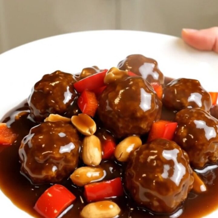 A top-down view of slow cooker kung pao meatballs with peanuts and red bell peppers.