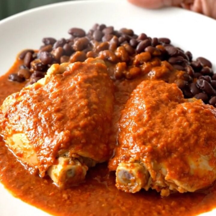 A close-up of tender chicken thighs covered in red enchilada sauce with black beans in a slow cooker.