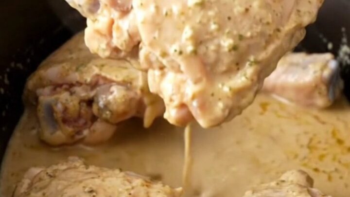 A close-up of tender, braised chicken thighs coated in a glossy, creamy ranch-based sauce in a slow cooker.