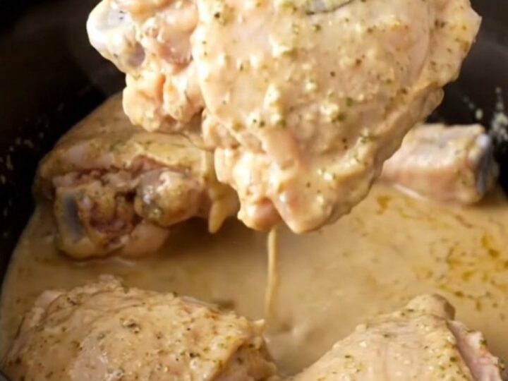 A close-up of tender, braised chicken thighs coated in a glossy, creamy ranch-based sauce in a slow cooker.