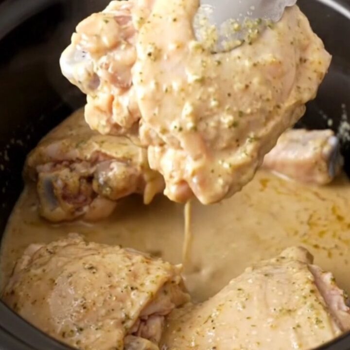 A close-up of tender, braised chicken thighs coated in a glossy, creamy ranch-based sauce in a slow cooker.