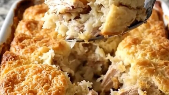 A golden, bubbling honey butter chicken biscuit bake in a white ceramic dish on a speckled countertop.