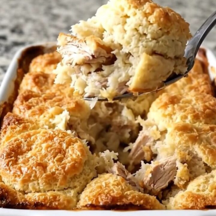 A golden, bubbling honey butter chicken biscuit bake in a white ceramic dish on a speckled countertop.