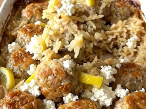 A rustic rectangular ceramic dish filled with golden baked rice, juicy chicken meatballs, and sprinkled feta cheese.