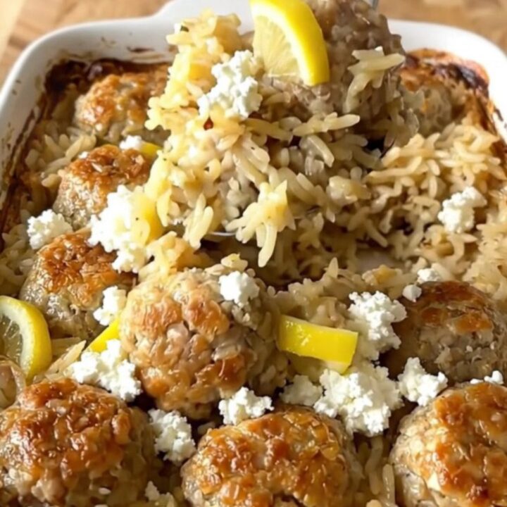 A rustic rectangular ceramic dish filled with golden baked rice, juicy chicken meatballs, and sprinkled feta cheese.