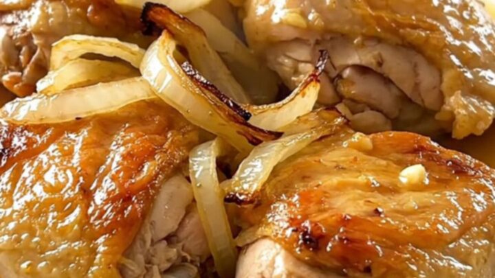 A close-up of tender, braised mojo chicken thighs topped with softened onions and citrus sauce on a white plate.