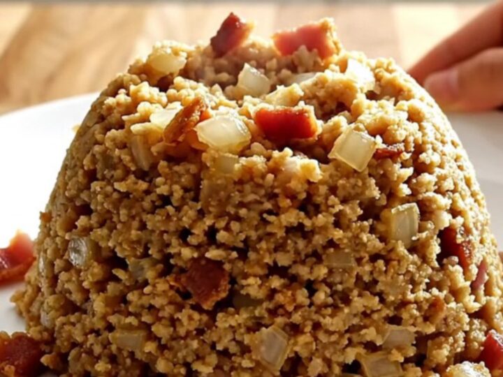 A white slow cooker filled with golden, savory bacon and onion stuffing on a wooden butcher-block counter.