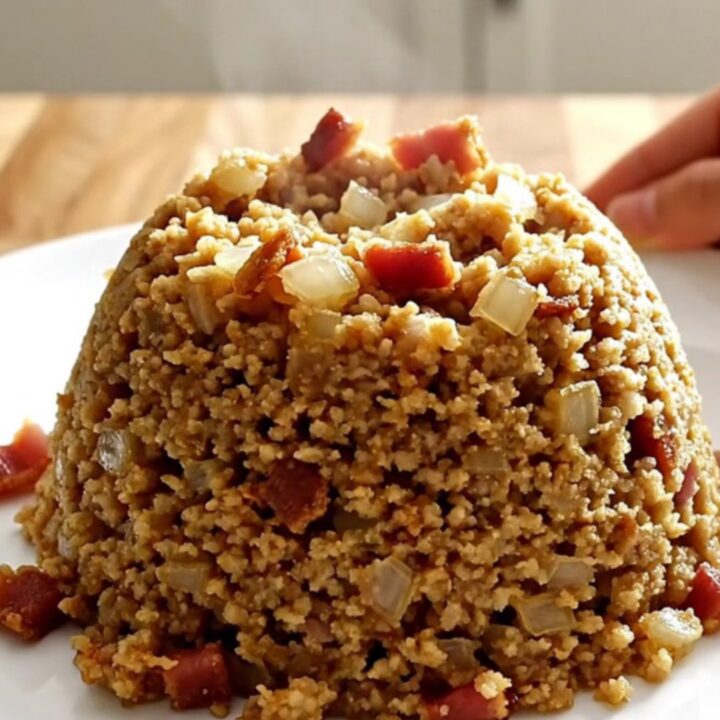 A white slow cooker filled with golden, savory bacon and onion stuffing on a wooden butcher-block counter.