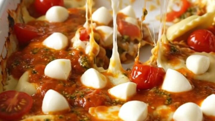 A top-down view of a rectangular ceramic dish filled with cheese ravioli, cherry tomatoes, pesto sauce