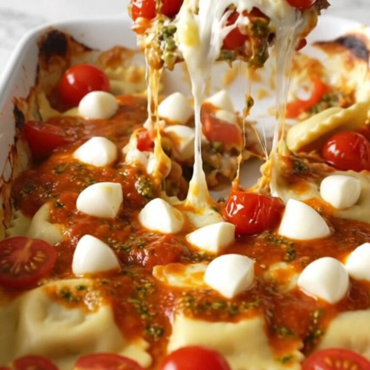 A top-down view of a rectangular ceramic dish filled with cheese ravioli, cherry tomatoes, pesto sauce