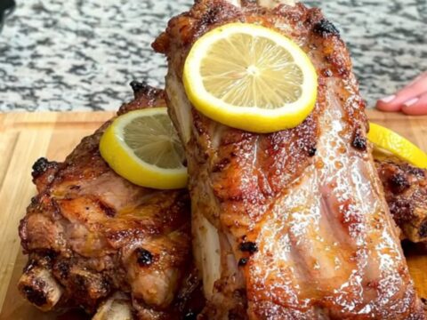Close-up of tender lemon pepper butter spareribs on a wooden board with visible lemon slices and juices.