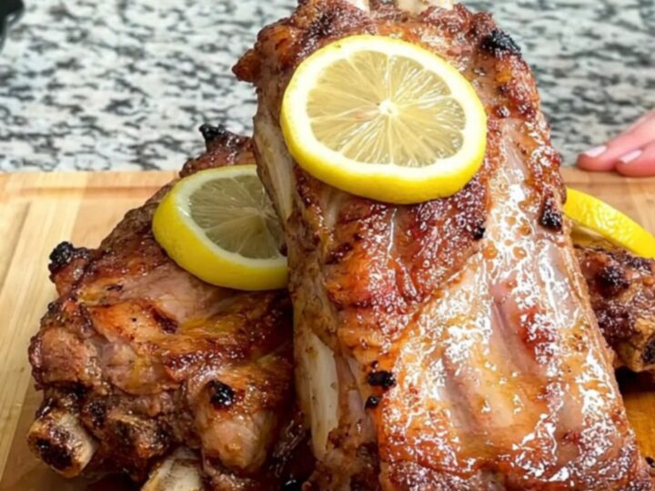 Close-up of tender lemon pepper butter spareribs on a wooden board with visible lemon slices and juices.