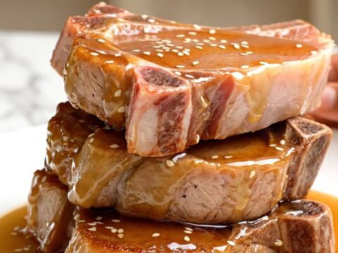 A close-up view of tender, braised pork chops coated in a glossy honey soy glaze, topped with sesame seeds.