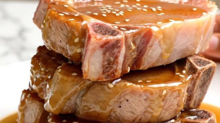 A close-up view of tender, braised pork chops coated in a glossy honey soy glaze, topped with sesame seeds.