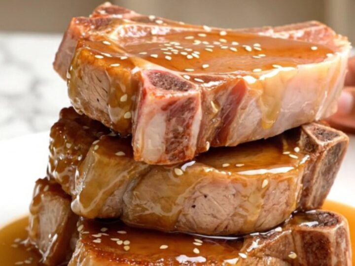 A close-up view of tender, braised pork chops coated in a glossy honey soy glaze, topped with sesame seeds.
