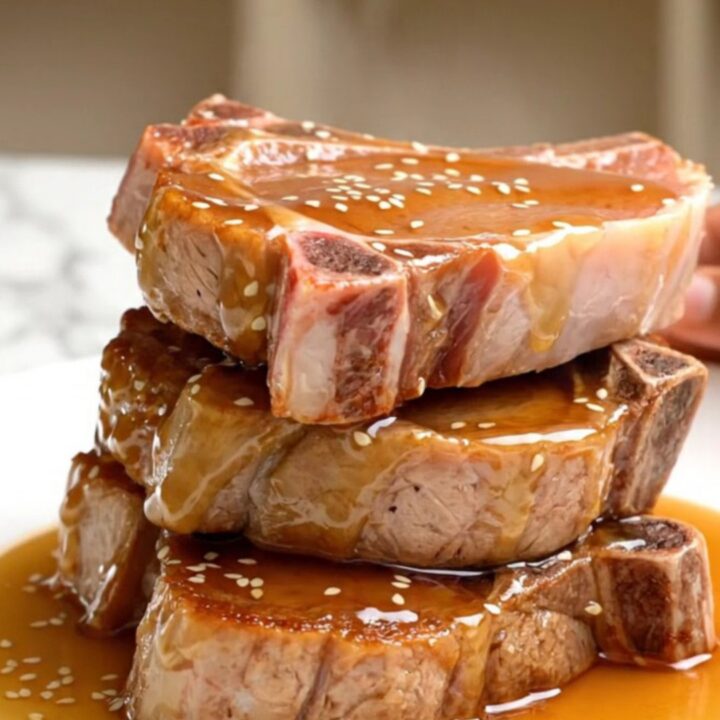 A close-up view of tender, braised pork chops coated in a glossy honey soy glaze, topped with sesame seeds.