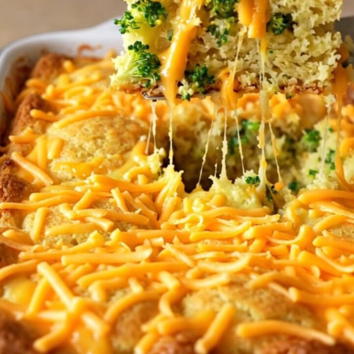 A golden-brown broccoli cheddar cornbread bake in an enameled rectangular dish on a beige countertop.
