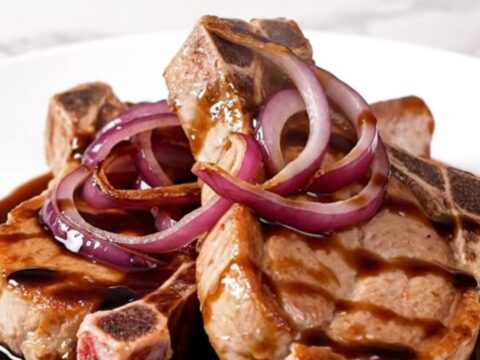 A close-up of tender, braised pork chops topped with caramelized red onions and a rich, dark balsamic sauce.