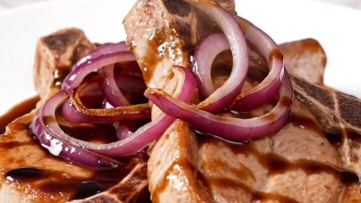 A close-up of tender, braised pork chops topped with caramelized red onions and a rich, dark balsamic sauce.
