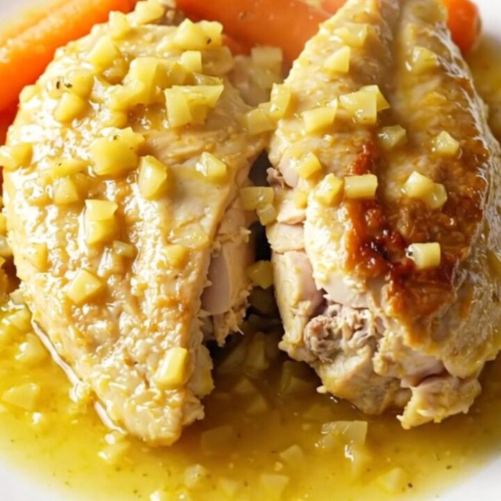A white plate featuring tender, braised chicken breasts and bright orange baby carrots in a lemon garlic sauce.