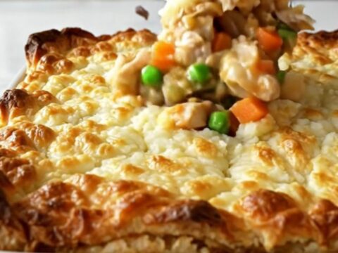 A golden-brown chicken shepherd's pie in a white ceramic dish, showing bubbling gravy and a textured potato topping.