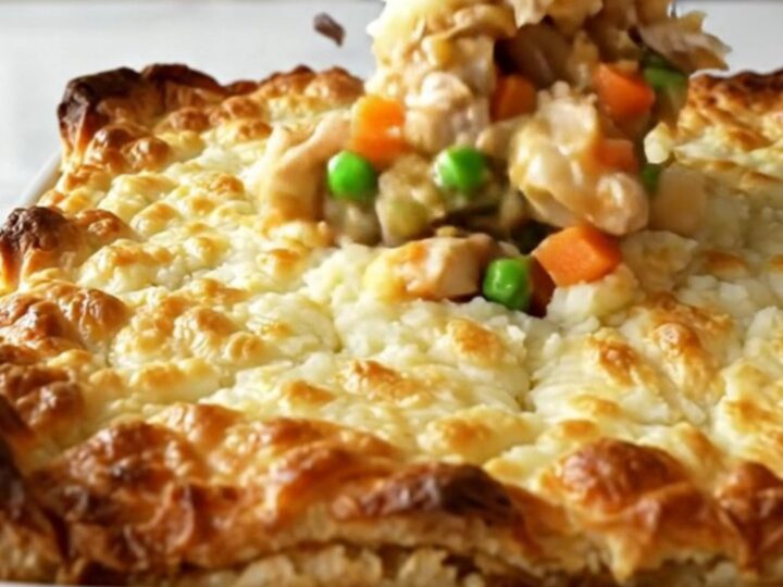 A golden-brown chicken shepherd's pie in a white ceramic dish, showing bubbling gravy and a textured potato topping.