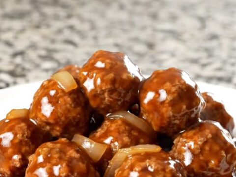 A top-down view of frozen beef meatballs being added to a black slow cooker on a granite countertop.