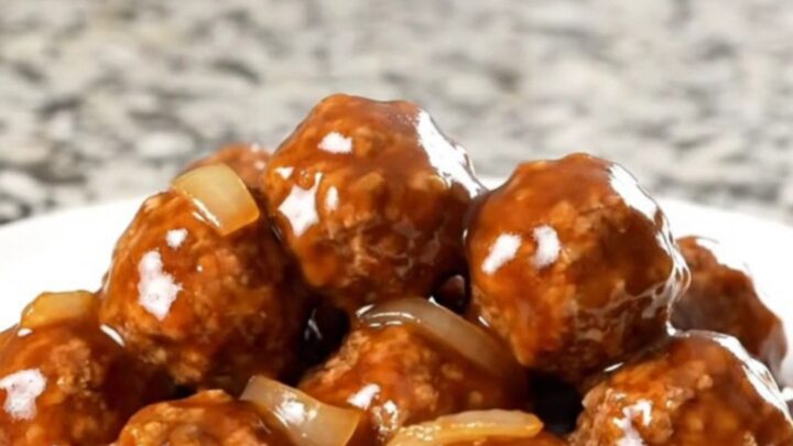 A top-down view of frozen beef meatballs being added to a black slow cooker on a granite countertop.