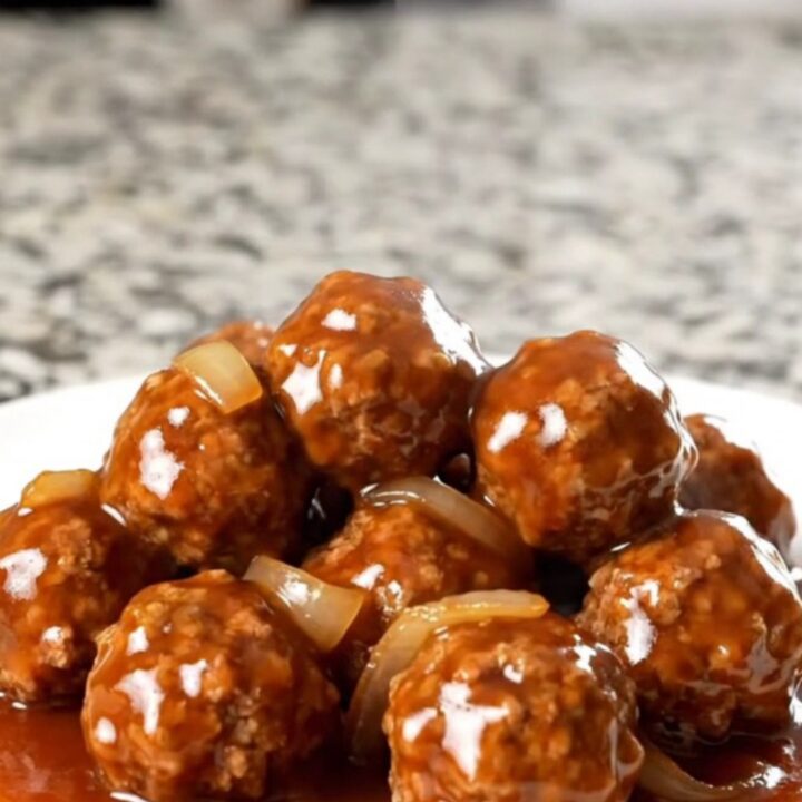 A top-down view of frozen beef meatballs being added to a black slow cooker on a granite countertop.