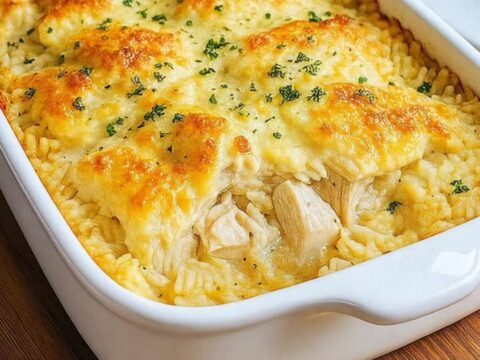 A golden-brown chicken and rice casserole in a white baking dish on a wooden counter.