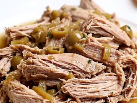 A close-up of tender, shredded pork loin with pickled giardiniera vegetables in a white bowl.