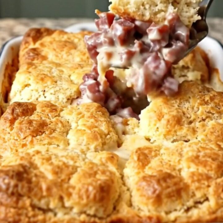 A golden-brown creamed chipped beef biscuit bake in a rectangular white enameled dish.