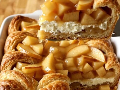A golden-brown apple danish crescent bake in a white ceramic dish.