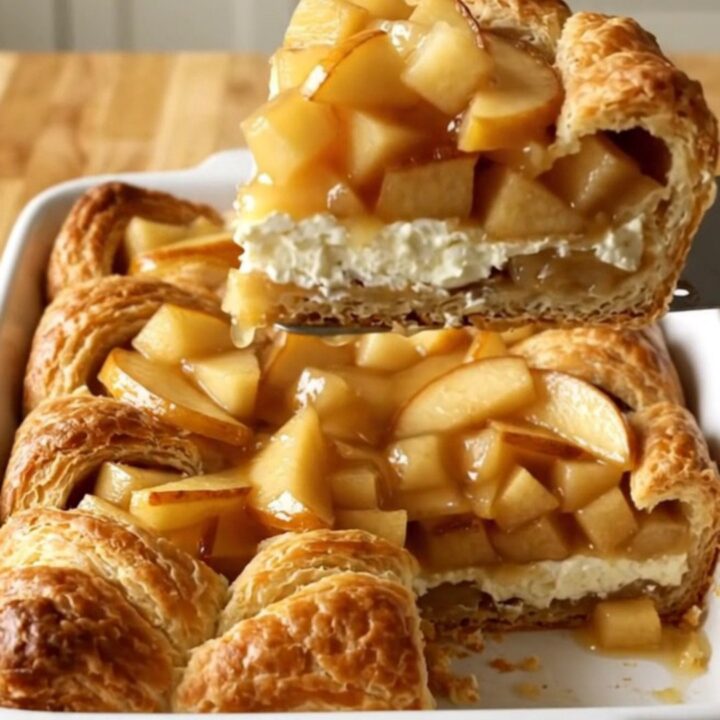 A golden-brown apple danish crescent bake in a white ceramic dish.