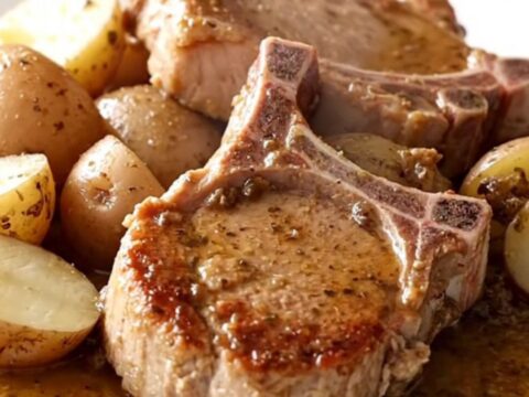 A close-up of tender bone-in pork chops and halved red potatoes in a savory broth inside a slow cooker.