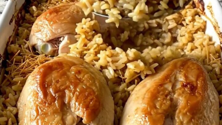 A top-down view of raw chicken breasts arranged over uncooked rice and vermicelli in a white rectangular baking dish.