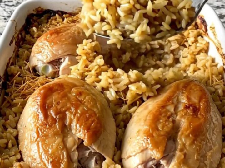 A top-down view of raw chicken breasts arranged over uncooked rice and vermicelli in a white rectangular baking dish.