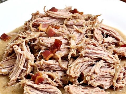 A close-up of creamy, shredded pulled pork with visible bits of bacon and a rich ranch-based sauce in a black slow cooker.