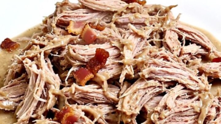 A close-up of creamy, shredded pulled pork with visible bits of bacon and a rich ranch-based sauce in a black slow cooker.