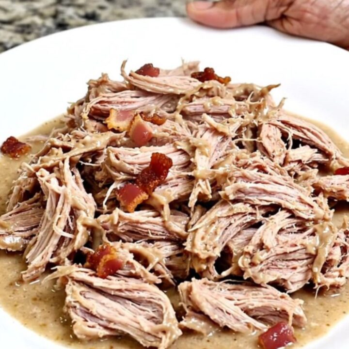 A close-up of creamy, shredded pulled pork with visible bits of bacon and a rich ranch-based sauce in a black slow cooker.