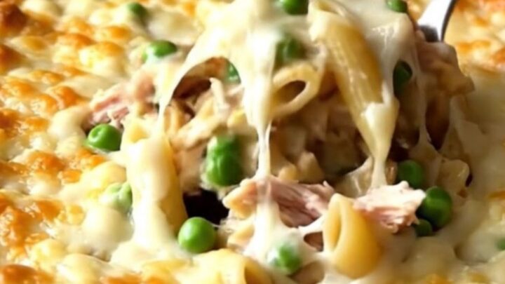 A large ceramic baking dish filled with creamy alfredo penne, turkey, and peas, topped with melted golden cheese.