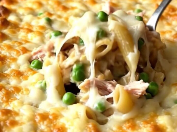 A large ceramic baking dish filled with creamy alfredo penne, turkey, and peas, topped with melted golden cheese.