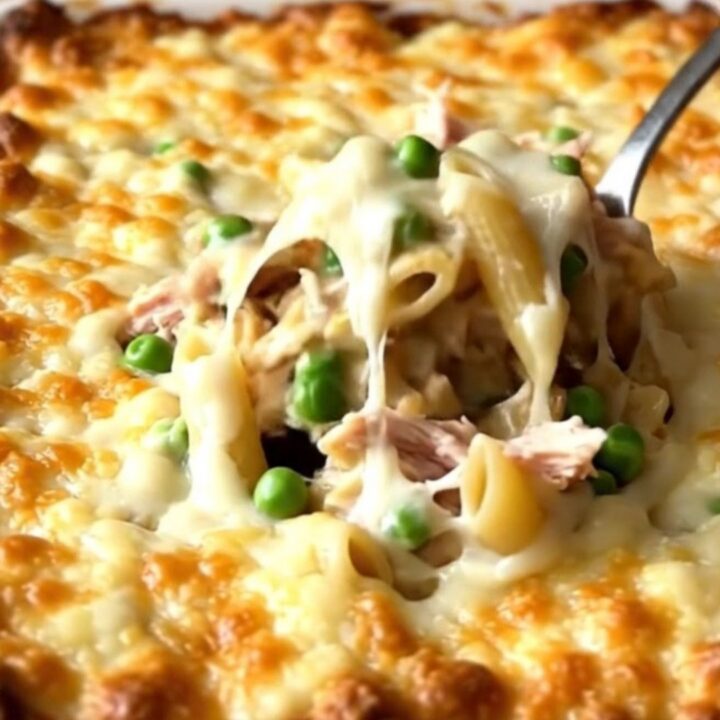 A large ceramic baking dish filled with creamy alfredo penne, turkey, and peas, topped with melted golden cheese.
