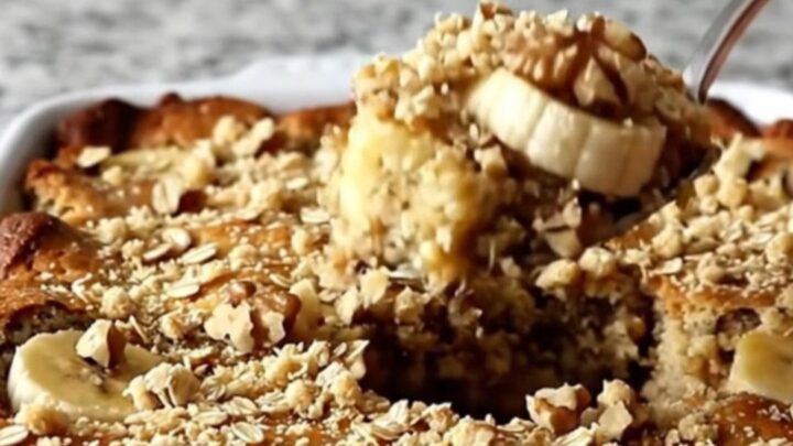 A golden brown banana bread cobbler in a ceramic dish, topped with a crunchy layer of oats and walnuts.