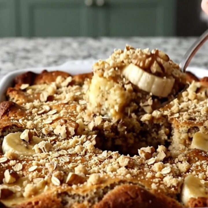 A golden brown banana bread cobbler in a ceramic dish, topped with a crunchy layer of oats and walnuts.