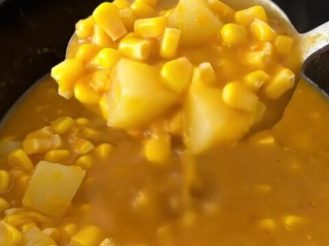 A close-up of a bowl of creamy pumpkin corn chowder with gold potato cubes and corn, garnished with herbs.