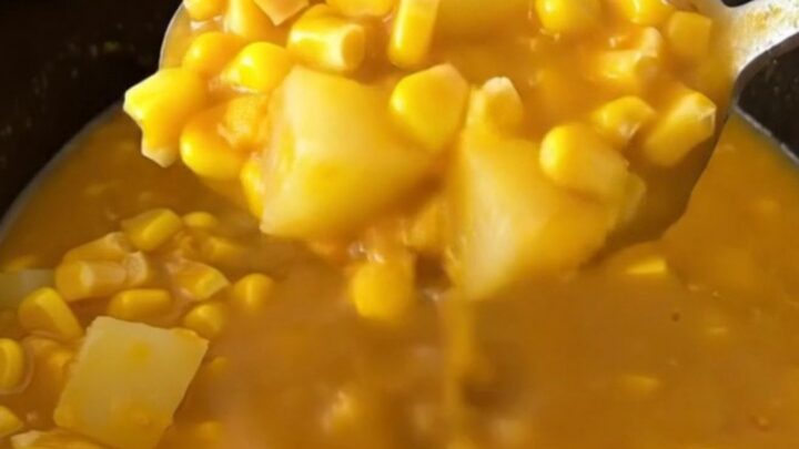 A close-up of a bowl of creamy pumpkin corn chowder with gold potato cubes and corn, garnished with herbs.