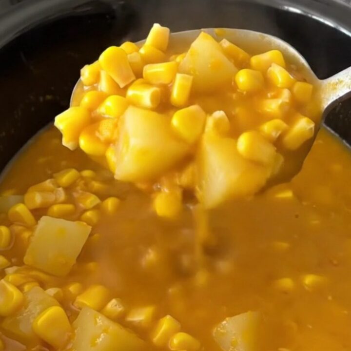 A close-up of a bowl of creamy pumpkin corn chowder with gold potato cubes and corn, garnished with herbs.