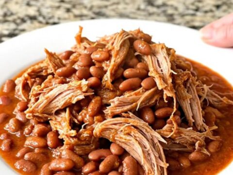 A slow cooker filled with a tender pork shoulder roast, pinto beans, and a flavorful red chili-tomato sauce.