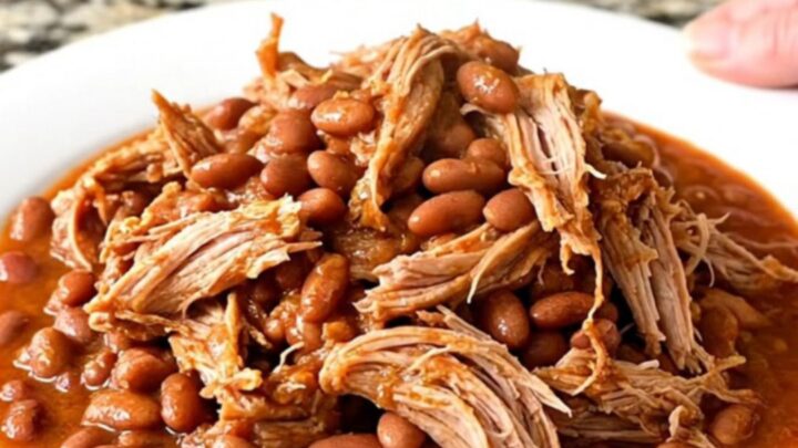 A slow cooker filled with a tender pork shoulder roast, pinto beans, and a flavorful red chili-tomato sauce.